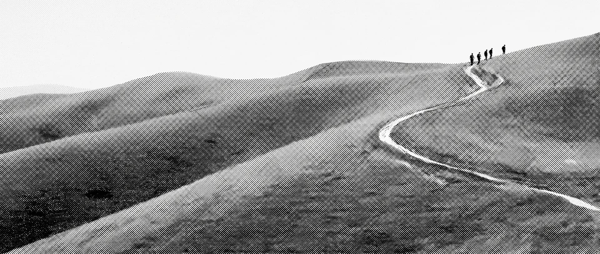Colline ondulate a strati con un sentiero chiaro che sale serpeggiando e alcune figure in cammino verso il crinale.